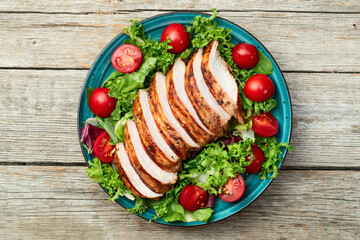 Grilled chicken breast ( fillet ) with lattuce salad and cherry tomatoes . Top view