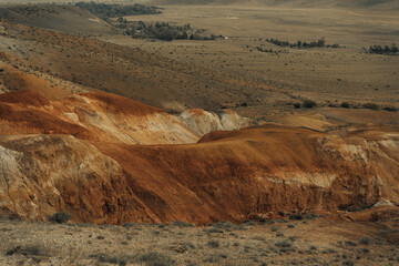 Vibrant hues of red and orange adorn the rugged terrain of the Altai Mountains at twilight, showcasing nature’s artistic beauty in this remote area