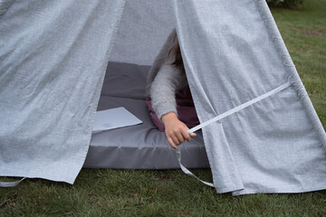 Hand of little girl playing and hiding in textile toy wigwam in garden at summer day © Natalia Navodnaia