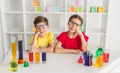 Two children wearing safety goggles conducting science experiments with colorful liquids in beakers and test tubes in a laboratory setting.