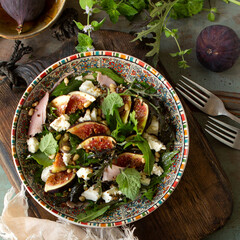 bowl of salad with prosciutto, figs and feta cheese on table