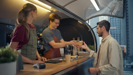Caucasian Customer Enjoying Buying Takeaway Coffee and Snacks From a Trendy Street Cafe in a Bustling City. Barista Serves Order with a Smile, Client Pays by Card Connected to His Smartphone