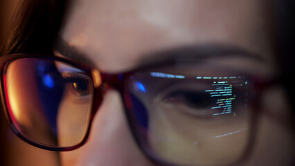 Close-up of a developer wearing glasses, coding on a computer. Code and analytics reflections in the glasses emphasize focus on cybersecurity and software development.