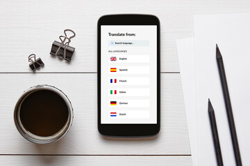 Overhead view of a smartphone displaying a language translator app, surrounded by office supplies on a white wooden desk.