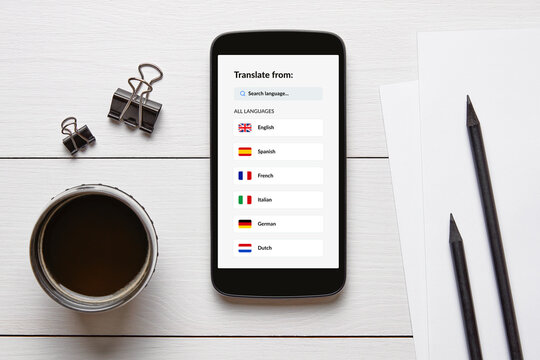 Overhead view of a smartphone displaying a language translator app, surrounded by office supplies on a white wooden desk.