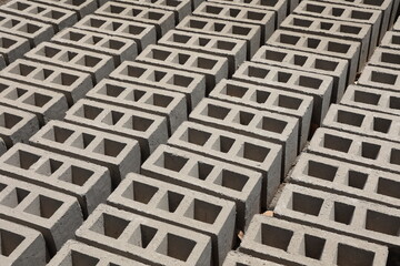 Rangées de parpaings creux gris en ciment, formés de trois alvéoles, et séchant sur le sol. Matériaux de construction constitués de blocs alignés formant une surface rugueuse. Photo prise au Sénégal.