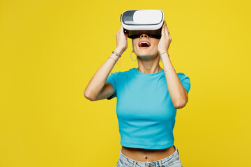 Young surprised amazed shocked Latin woman she wears blue top t-shirt headband casual clothes watching in vr headset pc gadget isolated on plain yellow background studio portrait. Lifestyle concept.