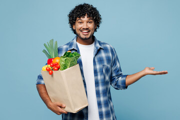 Young fun happy Indian man wear shirt hold brown craft bag for takeaway mock up with food products...