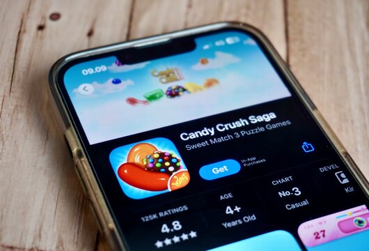 Jakarta, Indonesia - August 22th, 2024 - Candy crush saga match 3 puzzle game mobile application on app store phone screen isolated on horizontal wooden surface background.