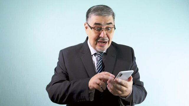 A businessman in a suit looks at his phone and celebrates happily, screaming with happiness and raising his hands in gratitude for a successful business venture. The concept of luck, triumph and grati