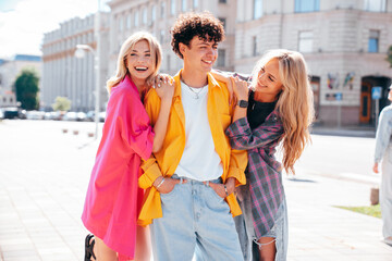 Group of young three stylish friends posing in the street. Fashion man and two cute female dressed in casual summer clothes. Smiling models having fun. Cheerful women and guy outdoors