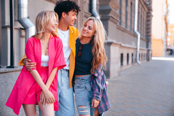 Fototapeta premium Group of young three stylish friends posing in the street. Fashion man and two cute female dressed in casual summer clothes. Smiling models having fun. Cheerful women and guy outdoors