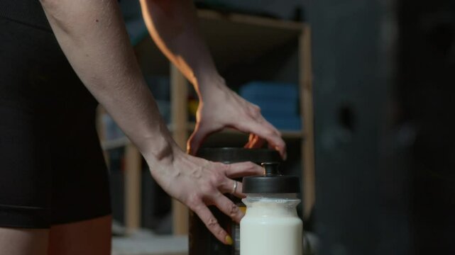 Close up shot of unrecognisable athletic girl adding one measuring spoon of protein powder to milk and shaking gym bottle after workout