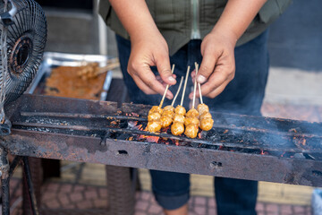 Street vendor grilling skewers of meatball-like food over charcoal
