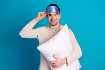 Photo of nice young man hold cushion wear pajama isolated on blue color background