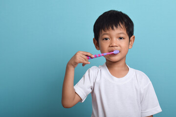 A happy Asian boy with clean teeth brushing his teeth isolated on blue background. Children's dental hygiene, Medical care