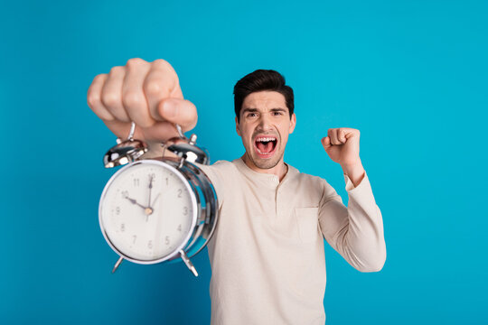 Photo of nice young man hold alarm raise fist wear pajama isolated on blue color background