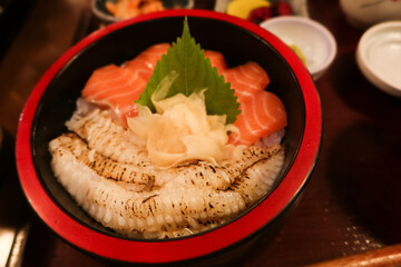 close up of Japanese raw seared salmon Flounder Sashimi fish rice in a black and red bowl donburi with ginger