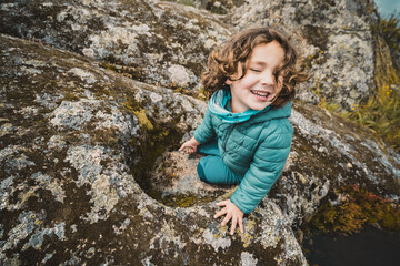 A young girl is sitting on a rock with her arms crossed and a smile on her face