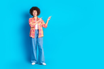 Full body photo of pretty young girl point empty space wear trendy plaid outfit isolated on blue color background