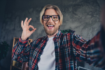 Selfie photo of young bearded blond hair business man in office making video showing okey symbol about his typical day at job workplace