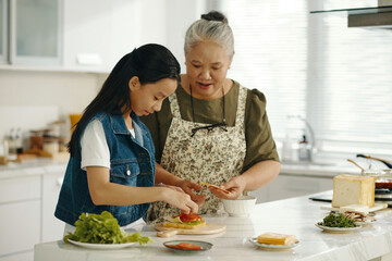 Grandma teaching her granddaughter to cook sandwich in the kitchen