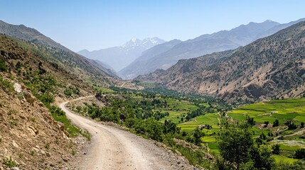 A narrow road winding through a mountainous landscape, surrounded by green valleys and peaks, under a clear sky.