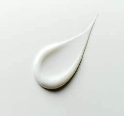 A single, small drop of white cosmetic cream on the surface of a flat and smooth white background