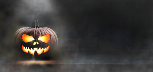 A scary spooky glowing carved halloween pumpkin lantern, Jack O' Lanterns, on the left of a wooden...