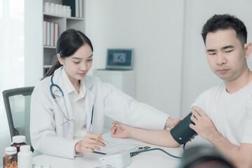 Asian female nurse talking and asking about symptoms of young male patient using blood pressure monitor to measure blood pressure level Medical examination result during consultation