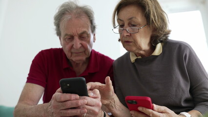 Elderly couple using smartphones together, sitting closely on a couch, both focused on their screens, showcasing technology use among seniors, collaboration, and modern communication in a home setting