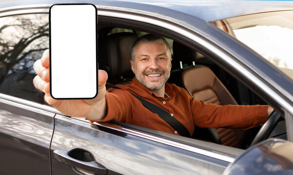 Excited middle aged man demonstrating big blank smartphone at camera, sitting in car, showing space for mobile offer, mockup