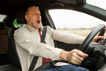 Frightened middle aged man screaming and braking just before an accident, driving car is about to...