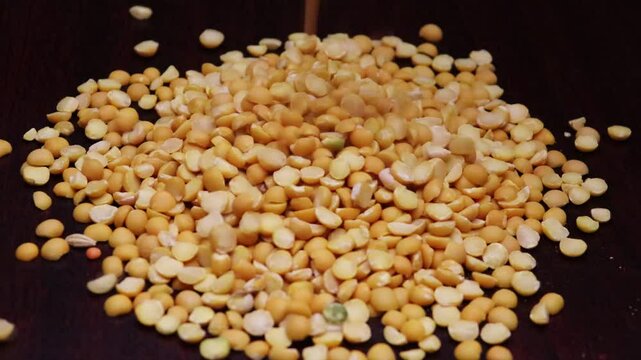 Dry yellow split peas drops from top to heap. Pigeon peas, Arhar legume split on black board. Toor dal (India), Congo pea drops on table close up video.