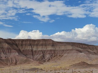 Brown Striped Painted Desert Hill under Bright Blue Sky and Fluffy White Clouds in Summer in Arizona United States