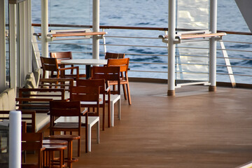 Outdoor seats on passenger ship deck with the calm seascape. Cruise ship deck. Wooden promenade deck on a luxury cruise liner. Ocean in background.