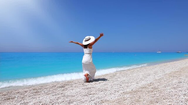 A tourist woman in a white summer dress enjoys the beautiful Egremni beach with turquoise sea at the island of Lefkada, Greece