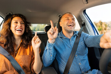 Car trip concept. Positive European spouses having fun while driving auto, couple listening to music and dancing, shot from dashboard