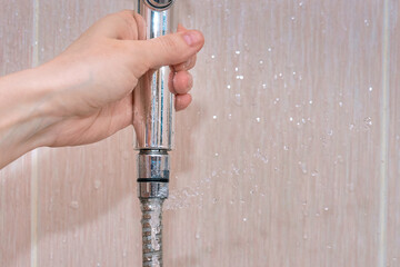 Laaking water hose close to shower head, water flow from the hole of the hose closeup. Broken...