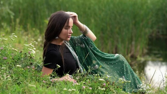 Beautiful  brunette extra long braided hair girl in Indian traditional dress posing near river . Portrait of young attractive stylish woman in sari on  green nature background.