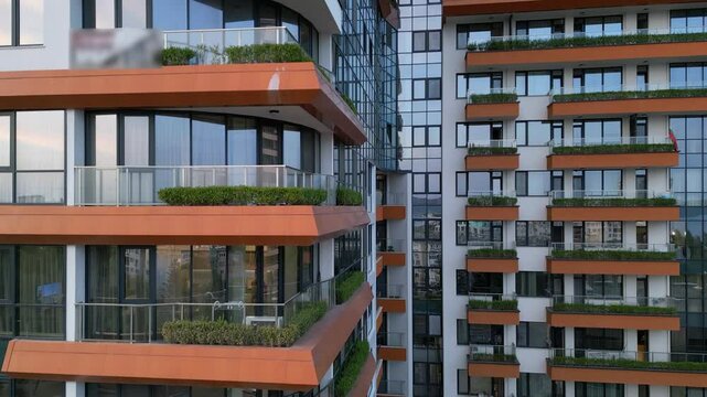 Aerial drone shot showcasing a modern apartment building's facade with vibrant orange accents and green balconies, emphasizing urban architecture and contemporary living