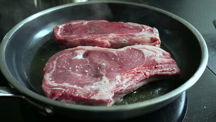 Raw steaks sizzling in a hot pan, lightly salted, beginning to cook, close-up view of fresh beef, home cooking process, preparing a delicious meal, culinary detail, kitchen scene