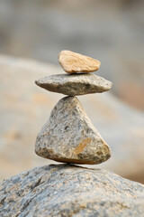 A carefully balanced stack of three stones on a rocky surface, symbolizing harmony and stability in a natural outdoor setting.