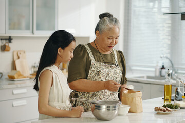 Grandma preparing dough together with her granddaughter and teaching her to bake