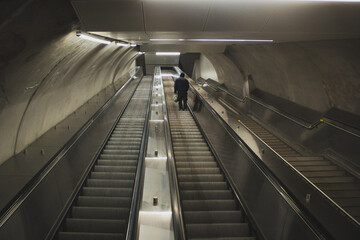 Obraz premium Wide angle photograph of a lone man ascending an empty escalator in an underground subway during the early morning hours.