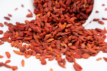 Dried goji berries spilled out of a plate on a white background.