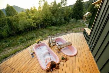 A soothing bubble bath in pink bathtubs set on a wooden deck, overlooking a lush green forest in...