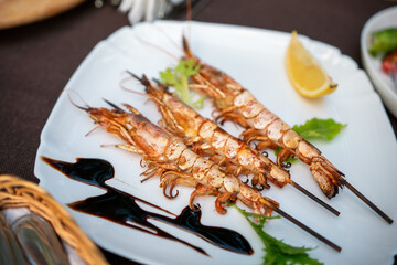 Shrimp Skewers Lemon Sauce Plate - Grilled shrimp skewers on a white plate with lemon wedges, sauce and greens.