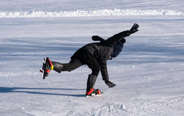 Boy in black winter clothes and on colorful skates slips, loses his balance and falls on the ice,...
