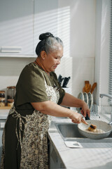 Asian housemaid washing dishes after cooking in the kitchen